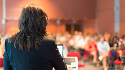 Image of female speaking to audience in a large room
