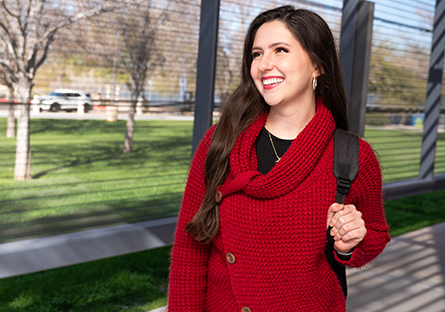 A happy, smiling student wearing a red sweater and backpack standing outside
