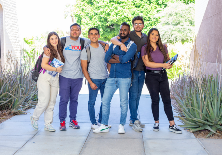 Six college students standing together  outside wearing backpacks and holding books