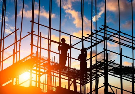 Stock photo of construction workers standing on scaffolding as the sun rises