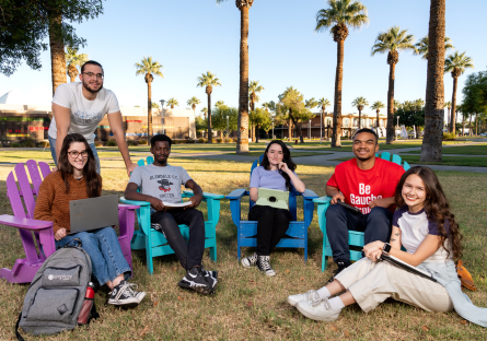 Four GCC students sitting outside in chairs and one sitting on the grass at the college campus