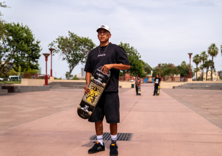 Douglas Miles Jr. holds a skateboard at a skate park.
