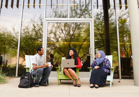 Three students sitting outside working on their laptops