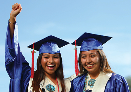 Image of two  female Native American graduates wearing cap and gown