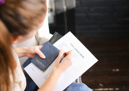 An image of a woman holding a passport and completing Visa form
